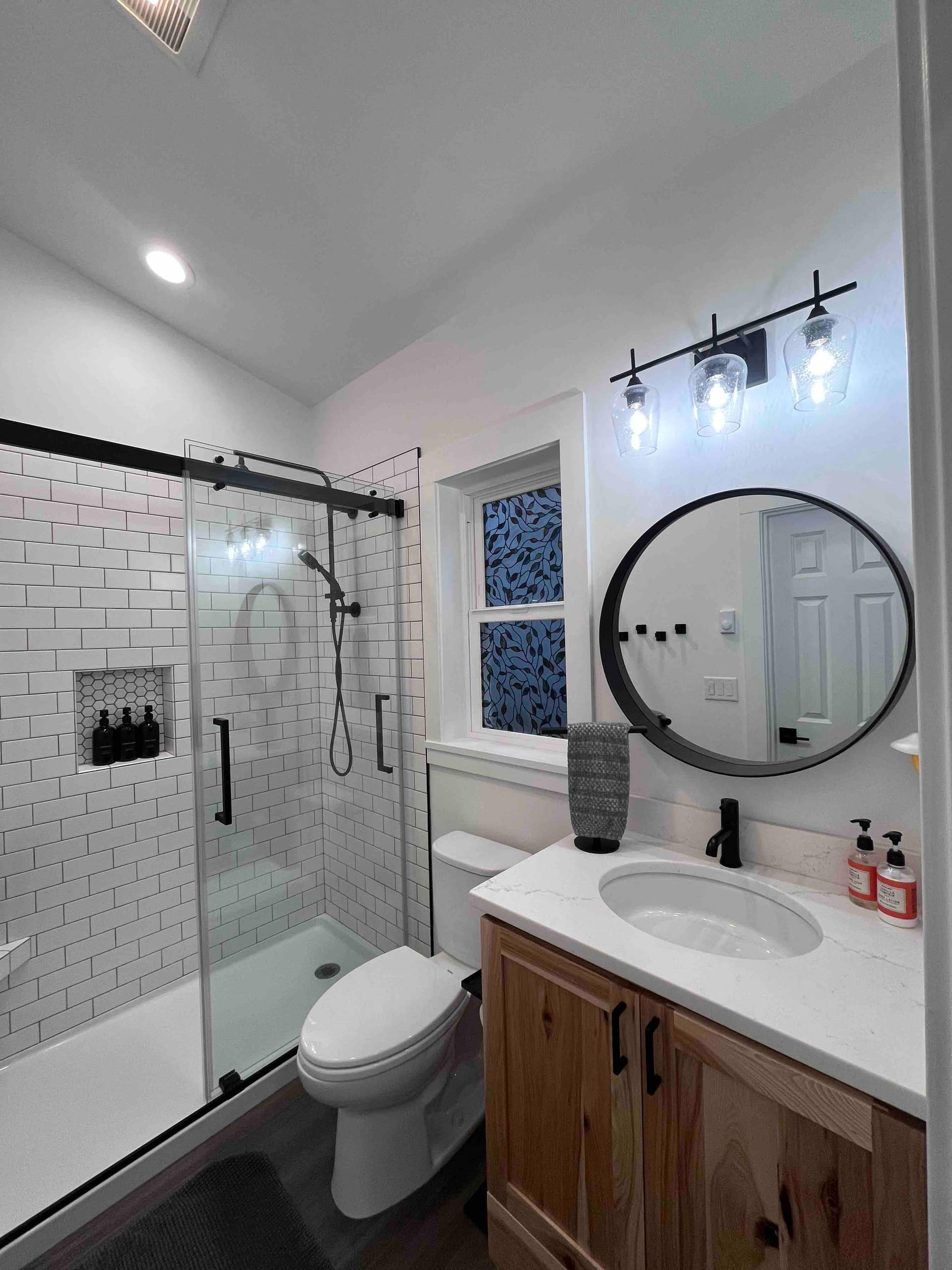 Bright full bathroom with a glass shower and round mirror